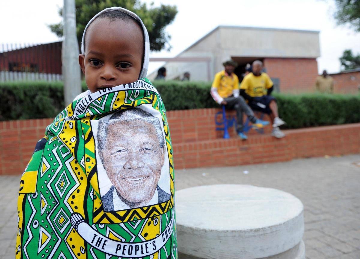 A child draped in a cloth with the image of former South African president Nelson Mandela, stands outside his former home, now museum, in Soweto, South Africa, Friday, Dec. 6, 2013. 