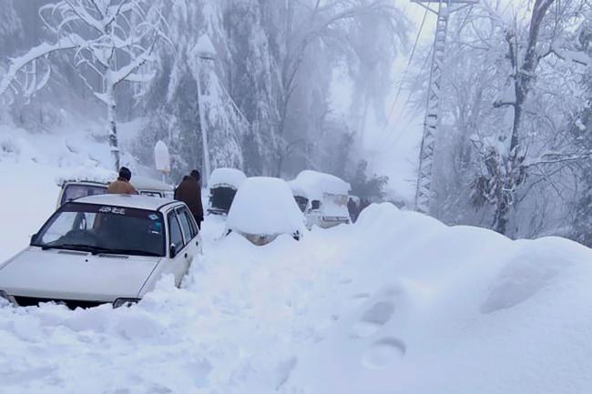 People walk past vehicles trapped in heavy snow in Murree